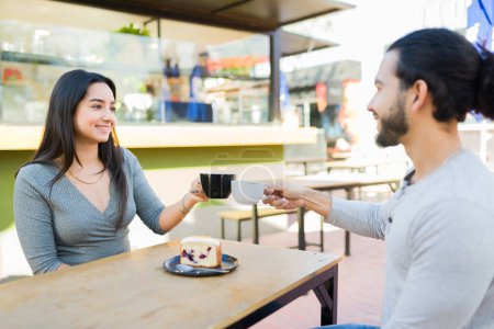 Téléchargez les photos : Heureux couple attrayant dans la vingtaine souriant ayant un rendez-vous romantique au café en plein air et boire du café avec dessert - en image libre de droit