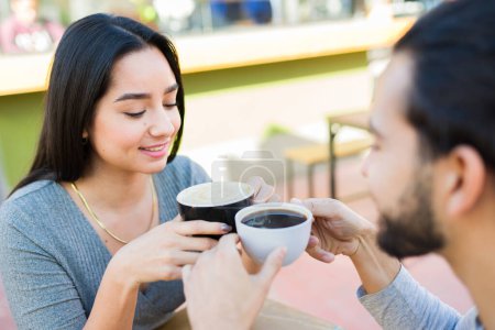 Foto de Atractiva joven mujer y hombre latino sonriendo y disfrutando tomando café juntos durante una cita en el café - Imagen libre de derechos