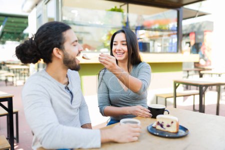 Téléchargez les photos : Jeune femme excitée nourrissant son petit ami heureux lors d'un rendez-vous romantique mangeant un dessert sur un rendez-vous café - en image libre de droit