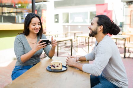 Téléchargez les photos : Jolie jeune femme riant à un rendez-vous amusant avec son petit ami boire du café et manger un dessert au café en plein air - en image libre de droit