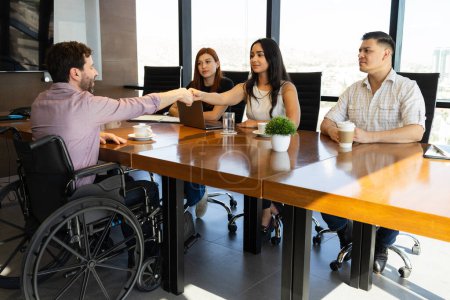 Photo for Three people of human resources interviewing a candidate on a wheelchair and shaking his hand - Royalty Free Image