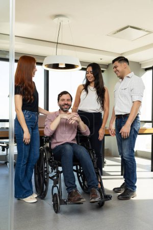 Téléchargez les photos : Portrait d'un homme handicapé heureux dans un fauteuil roulant entouré de personnes qui le soutiennent dans un bureau inclusif - en image libre de droit