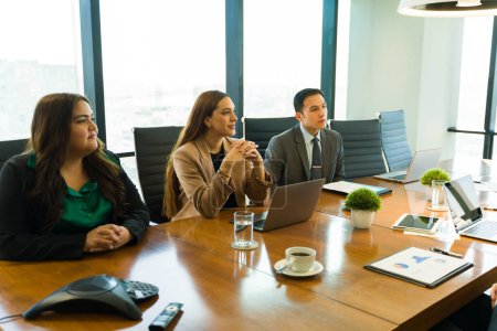 Téléchargez les photos : Groupe confiant de partenaires d'affaires assis dans une table de conférence et à l'écoute attentive d'une présentation - en image libre de droit