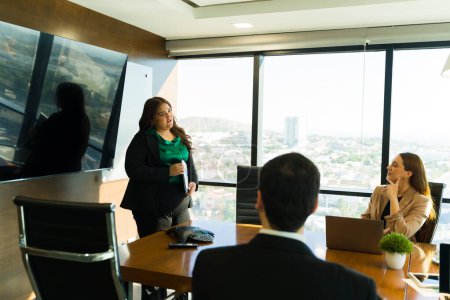 Foto de Hermosa empresaria hispana haciendo una presentación de ventas a algunos de sus clientes más importantes en una sala de reuniones - Imagen libre de derechos