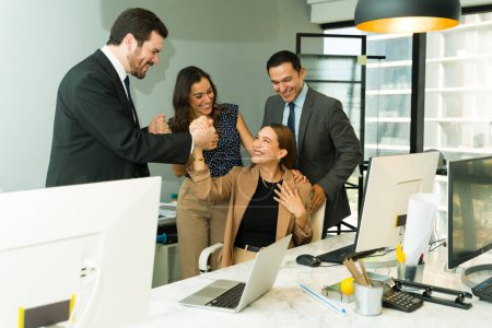 Foto de Hermosa mujer que se ve emocionada mientras recibe aliento y reconocimiento de sus colegas en una oficina - Imagen libre de derechos