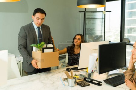 Photo for Businessman taking his stuff and leaving the office while others watch him after getting laid off - Royalty Free Image