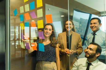 Téléchargez les photos : Les hommes d'affaires s'amusent en utilisant des notes collantes dans un mur de verre lors d'une activité de team building - en image libre de droit