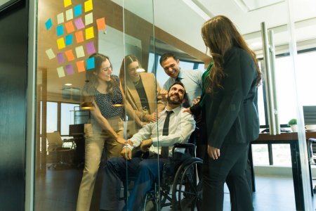 Photo for Man in a wheelchair getting recognized and congratulated by his coworkers in a meeting room - Royalty Free Image