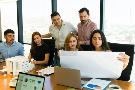 Photo for Diverse group of architects working on a building project and examining a model and some plans - Royalty Free Image