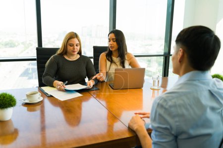 Photo for Two female recruiters looking at a candidate's resume and discussing his skills and experience in an interview - Royalty Free Image