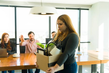 Photo for Portrait of an upset woman in casual clothing carrying a box with her belongings while leaving the office after getting fired - Royalty Free Image