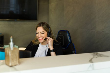 Foto de Hermosa recepcionista caucásica con auriculares y hablando con un cliente con una sonrisa - Imagen libre de derechos