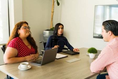 Photo for Couple of female recruiters paying attention to a man talking during a job interview in an office - Royalty Free Image