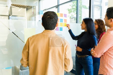 Téléchargez les photos : Vue arrière d'une équipe d'affaires utilisant des notes collantes sur un mur et travaillant ensemble dans un bureau - en image libre de droit