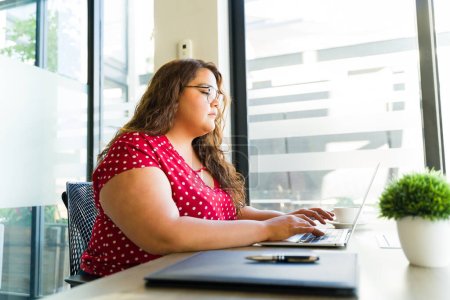 Foto de Mujer bastante gorda latina con gafas y trabajando en una computadora portátil en una sala de reuniones - Imagen libre de derechos