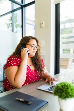 Foto de Hermosa mujer de negocios con sobrepeso ocupada en una llamada con un cliente mientras trabaja en una oficina - Imagen libre de derechos