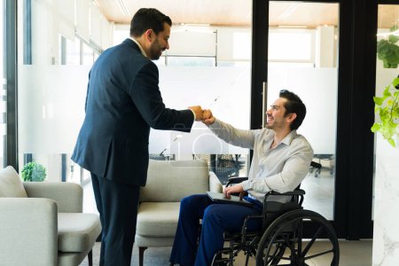 Téléchargez les photos : Homme d'affaires frappant les poings avec un travailleur handicapé dans un fauteuil roulant et se souriant - en image libre de droit