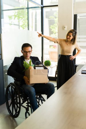 Photo for Sad Caucasian man in a wheelchair grabbing his stuff and leaving after being laid off from his job - Royalty Free Image