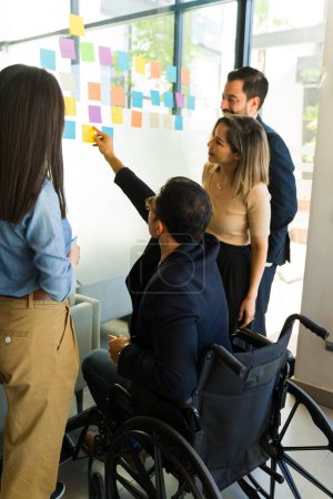 Foto de Vista trasera de un grupo de empresarios que utilizan notas adhesivas en una pared de vidrio en una sala de reuniones - Imagen libre de derechos