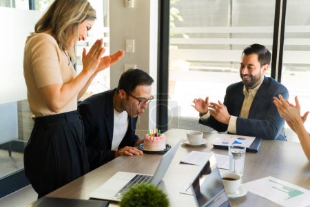 Foto de Grupo de empresarios aplaudiendo y celebrando mientras su jefe sopla las velas de un pastel de cumpleaños - Imagen libre de derechos