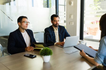 Photo for Two male recruiters sitting in a meeting room and interviewing a woman for a job - Royalty Free Image