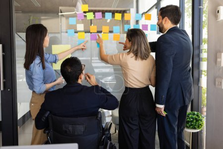 Photo for Rear view of a group of people using sticky notes as part of some team building activities - Royalty Free Image