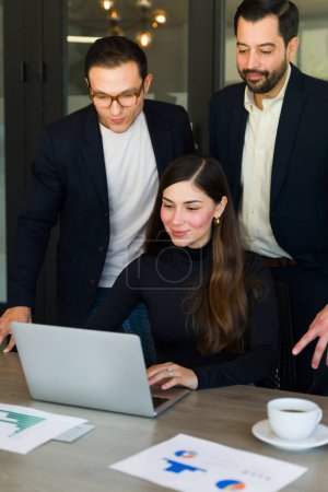 Téléchargez les photos : Jolie femme d'affaires hispanique montrant son travail sur un ordinateur portable à un groupe de gens d'affaires - en image libre de droit