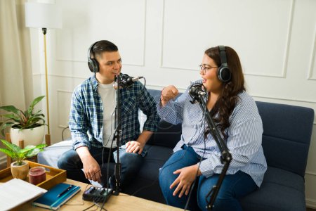 Foto de Feliz mujer latina grabando podcast con un hombre sonriente y un invitado mientras habla de una historia divertida - Imagen libre de derechos