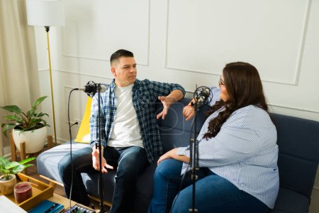 Foto de Hombre hispano y presentador de podcast hablando con una invitada durante un programa de entrevistas mientras graba un episodio - Imagen libre de derechos
