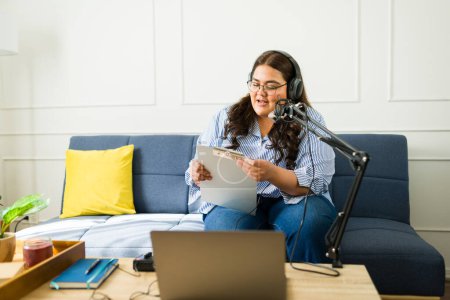 Foto de Mujer latina grabando un podcast amateur con micrófono y auriculares en la sala de estar - Imagen libre de derechos