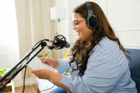 Photo for Attractive happy broadcaster woman smiling while reading listener's stories and recording a podcast episode - Royalty Free Image