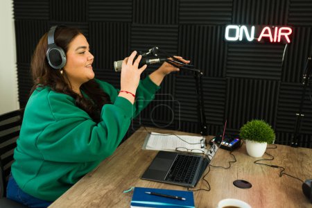 Téléchargez les photos : Broadcast femme se prépare à commencer son talk-show radio dans le studio insonorisé tout en enregistrant un podcast regardant heureux - en image libre de droit