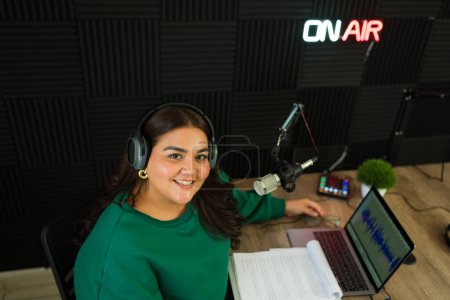 Téléchargez les photos : Vue de dessus d'un heureux animateur de radio hispanique ou podcaster souriant prêt à commencer l'enregistrement d'un épisode au studio - en image libre de droit