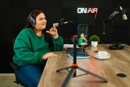 Téléchargez les photos : Heureuse femme latine enregistrant un épisode de podcast sur le studio insonorisé et filmant la vidéo ou le streaming en direct - en image libre de droit