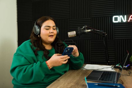Photo for Latin woman broadcaster with headphones on the recording studio at the radio station recording a podcast episode - Royalty Free Image