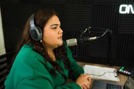 Téléchargez les photos : Animateur de podcast féminin avec écouteurs enregistrant un épisode de podcast et parlant d'une histoire lors d'une émission de radio - en image libre de droit