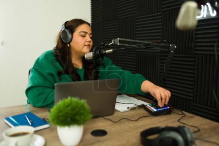 Photo for Latin woman preparing to start recording her radio talk show in the soundproof studio while using the audio mixer - Royalty Free Image
