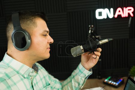 Photo for Attractive podcast host and podcaster getting ready the microphone and headphones at the soundproof studio to record an episode - Royalty Free Image