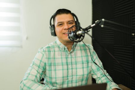 Téléchargez les photos : Beau homme heureux parlant sur le microphone tout en enregistrant un épisode de podcast parler d'une histoire amusante dans le studio - en image libre de droit