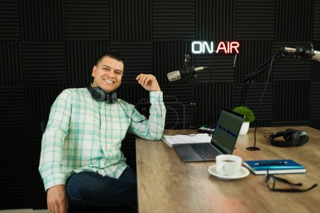 Photo for Excited hispanic man making eye contact and smiling having fun after recording a podcast episode in the soundproof studio - Royalty Free Image