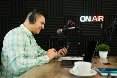 Photo for Latin broadcaster smiling while reading messages on social media on air while on his talk show on the radio - Royalty Free Image
