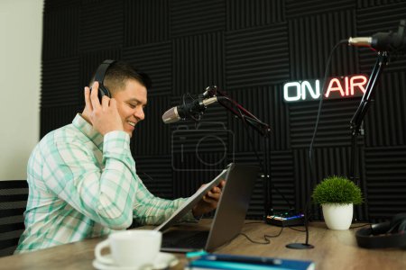 Photo for Happy man in his 30s smiling while reading a script story during a podcast episode or radio talk show - Royalty Free Image