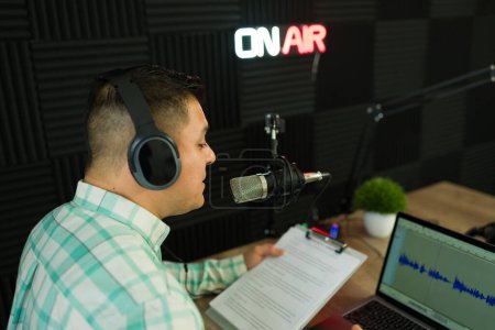 Photo for Broadcaster seen from behind hosting a podcast episode while reading a talk show script in the recording episode - Royalty Free Image