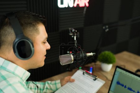 Photo for Rear view of a latin man with headphones talking to the microphone while recording a podcast episode or during a radio show - Royalty Free Image