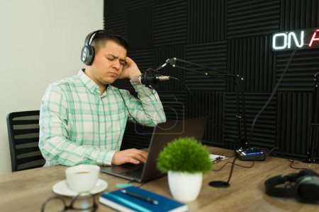 Photo for Attractive happy man listening to his favorite song with headphones while hosting a radio show or podcast episode with music - Royalty Free Image