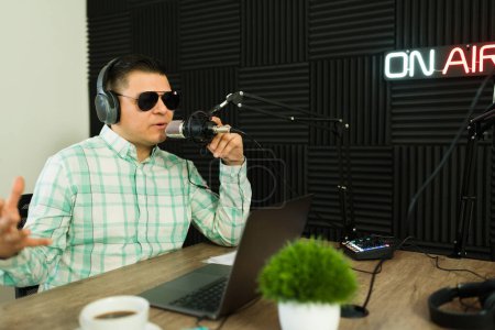 Téléchargez les photos : Hôte podcast joyeux avec des lunettes de soleil rire et s'amuser pendant son émission de radio tout en enregistrant en studio - en image libre de droit