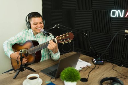 Téléchargez les photos : Joyeux homme heureux qui aime jouer de la musique avec une guitare tout en souriant dans le studio d'enregistrement insonorisé - en image libre de droit