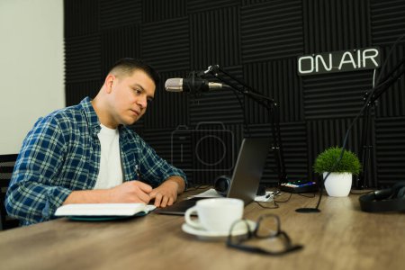 Photo for Busy latin man and broadcaster preparing to record his next podcast episode or radio show while at the soundproof studio - Royalty Free Image