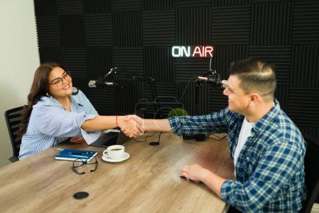 Photo for Excited beautiful woman shaking hands with her podcast guest and smiling before starting recording at the studio - Royalty Free Image