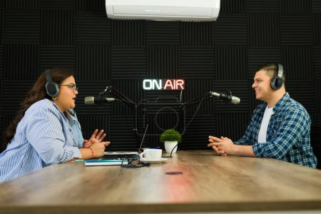 Photo for Cheerful podcast co-hosts smiling looking happy while recording an episode of their talk show at the radio studio - Royalty Free Image